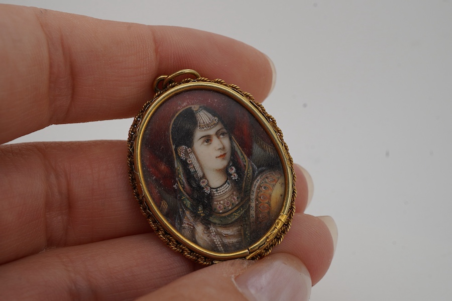 An ivory portrait miniature pendant, India, 19th century, depicting a woman in Mughal dress, in a gold mount with a rope twist chain border, to a pendant hoop, length 3.9cm, back damaged, later brooch fitting with pin de